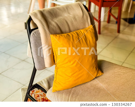 A chair with a yellow cushion and a beige blanket in the interior. A combination of warmth and practicality, a cozy detail in a modern space. Home comfort, interior, softness 130334267