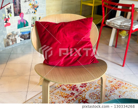 Wooden chair with a bright red pillow in the cafe interior. Cozy atmosphere, combination of simplicity and textile accent. Comfort, interior, minimalism 130334268