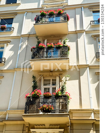 Residential building facade with balconies decorated by flowers and plants. Architectural detail symbolizing lifestyle, urban greenery and European heritage. Residential building facade with balconies decorated by flowers and plants. Architectural detail symbolizing lifestyle, urban greenery and European heritage. 130334284