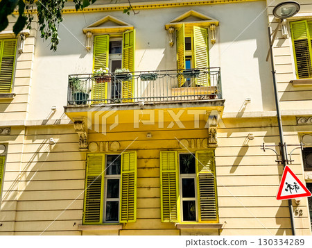 Historic building facade with yellow window shutters and balcony railing. Architectural detail symbolizing heritage, urban culture and European cityscape. Historic building facade with yellow window shutters and balcony railing. Architectural detail symbolizing heritage, urban culture and European cityscape. 130334289