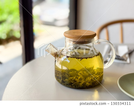 Glass teapot with herbal tea placed on cafe table. Warm beverage symbolizing relaxation, wellness and healthy lifestyle. Glass teapot with herbal tea placed on cafe table. Warm beverage symbolizing relaxation, wellness and healthy lifestyle. 130334311
