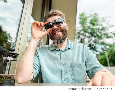 Glasses with magnetic clip on sunglasses. Man smiling while wearing clip on sunglasses at outdoor cafe table 130334343