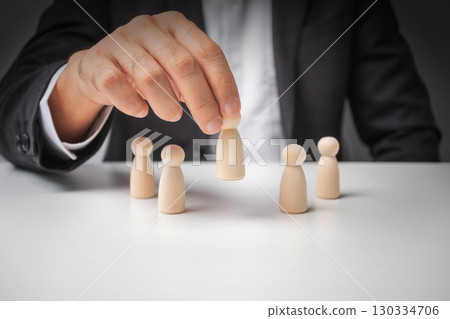 Businessman pick up leads from other wooden dolls on white desk. 130334706