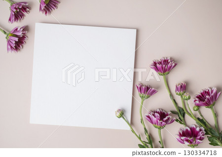White blank greeting or invitation card with purple flower decoration on beige background. 130334718