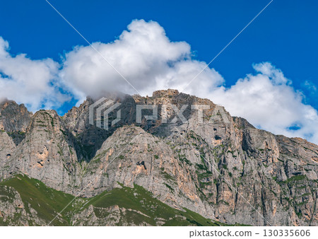 Stunning mountain landscape under vibrant blue sky with swirling clouds in the background Stunning mountain landscape under vibrant blue sky with swirling clouds in the background 130335606