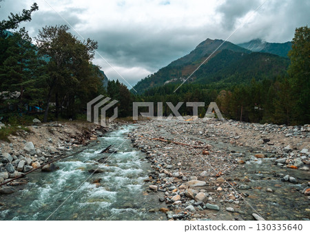 Serene river flowing through rocky landscape in mountains under overcast sky near forest 130335640