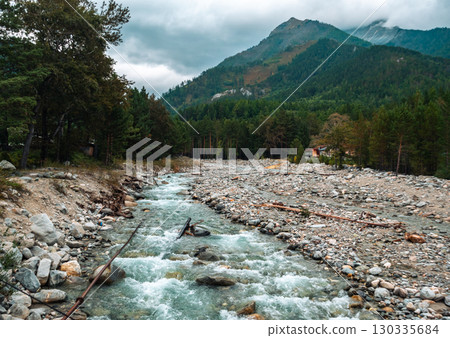 Serene river flowing through rocky landscape in mountains under overcast sky near forest Serene river flowing through rocky landscape in mountains under overcast sky near forest 130335684