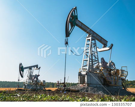 Oil pumps operate in a vast field under a clear blue sky at midday in rural area Oil pumps operate in a vast field under a clear blue sky at midday in rural area 130335707