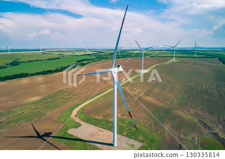 Wind turbines generate renewable energy in a wind farm located in a rural area under a clear sky during daylight hours Wind turbines generate renewable energy in a wind farm located in a rural area under a clear sky during daylight hours 130335814