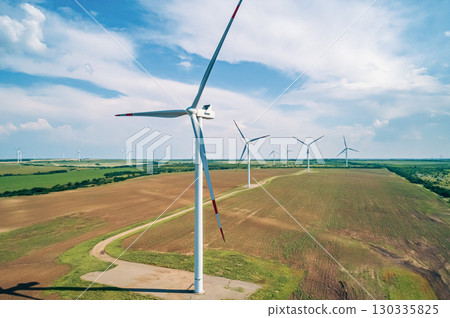 A row of large wind turbines stands tall in a vast, open field, showcasing renewable energy production. A row of large wind turbines stands tall in a vast, open field, showcasing renewable energy production. 130335825