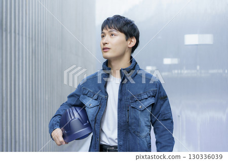 Portrait of a young man wearing denim work clothes and holding a helmet Portrait of a young man wearing denim work clothes and holding a helmet 130336039