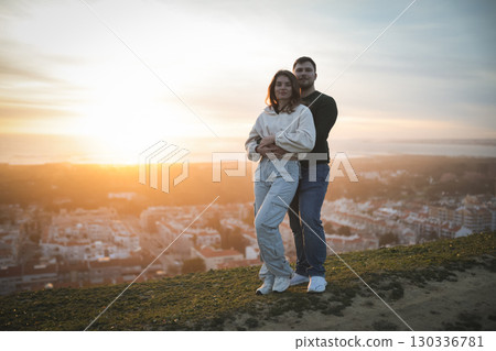 Couple embracing on hilltop overlooking city at sunset 130336781