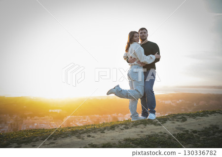 Young couple embracing on hilltop at sunset over cityscape 130336782