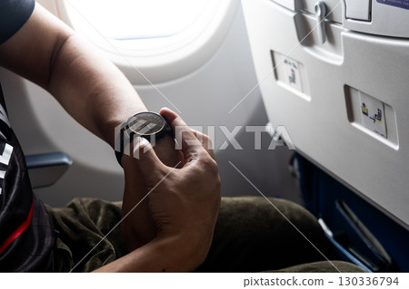 Passenger adjusting wrist watch to new time zone in airplane 130336794