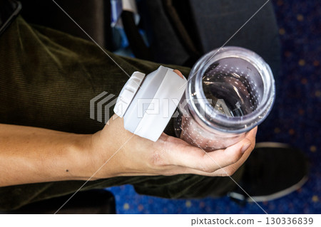 Hand holding empty transparent tumbler during travel to refill water in airplane for hydration Hand holding empty transparent tumbler during travel to refill water in airplane for hydration 130336839