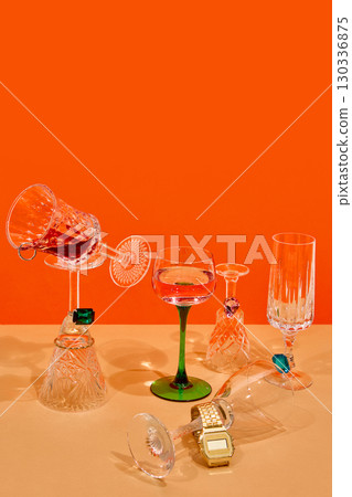 Conceptual still life of crystal glasses with rings and jewelry on orange background Conceptual still life of crystal glasses with rings and jewelry on orange background 130336875