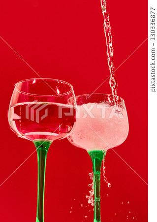 Artistic splash of drink pouring into cocktail glass on red backdrop with vibrant mood Artistic splash of drink pouring into cocktail glass on red backdrop with vibrant mood 130336877
