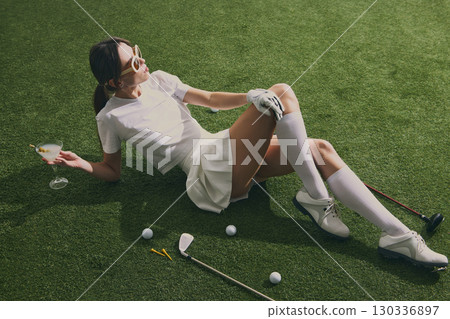Stylish golfer woman with cocktail relaxing on course grass Stylish golfer woman with cocktail relaxing on course grass 130336897