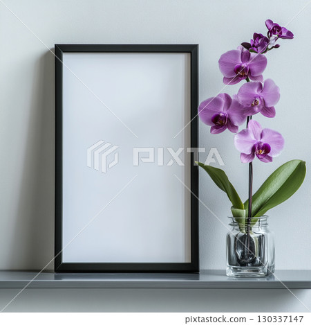 A simple, clean shot of a black-framed blank poster on a white shelf next to a vibrant purple orchid in a clear vase. It's a minimalist scene. 130337147