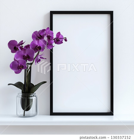 A simple, clean shot of a black-framed blank poster on a white shelf next to a vibrant purple orchid in a clear vase. It's a minimalist scene. 130337152