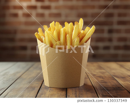 A cup of crispy, golden french fries stands upright on a rustic wooden table. The focus is on the delicious, fast-food snack against a dark, blurred background. 130337349