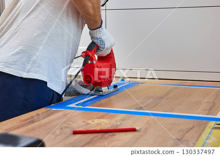 repairman using handheld electric jigsaw and cutting hole for the sink in the kitchen countertops, Woodworking and carpentry concept 130337497