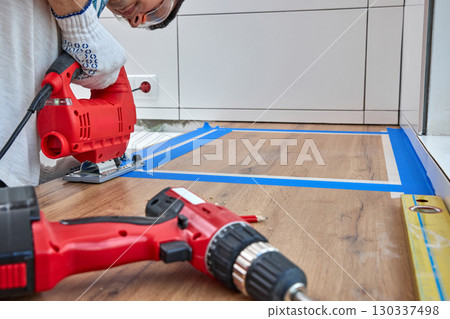repairman using electric jigsaw and cutting hole for the sink in the kitchen countertops, Woodworking and carpentry concept 130337498