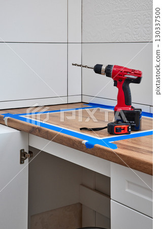 red cordless electric drill screwdriver and measuring tape on kitchen countertop. Kitchen cabinet installation red cordless electric drill screwdriver and measuring tape on kitchen countertop. Kitchen cabinet installation 130337500