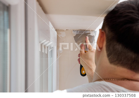 Caucasian plasterer man with a spatula applying finishing putty on a window opening 130337508
