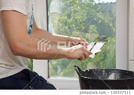 Caucasian plasterer man with a spatula applying finishing putty on a window opening Caucasian plasterer man with a spatula applying finishing putty on a window opening 130337511