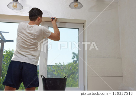 Caucasian plasterer man with a spatula applying finishing putty on a window opening Caucasian plasterer man with a spatula applying finishing putty on a window opening 130337513