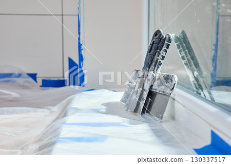 Kit of putty knives on white windowsill, copy space. Workplace. Construction tool. 130337517