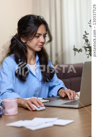 happy attractive woman in blue shirt working using laptop in home office happy attractive woman in blue shirt working using laptop in home office 130337529