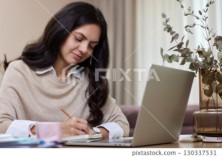 Happy positive woman using laptop while working remotely from home in living room Happy positive woman using laptop while working remotely from home in living room 130337531