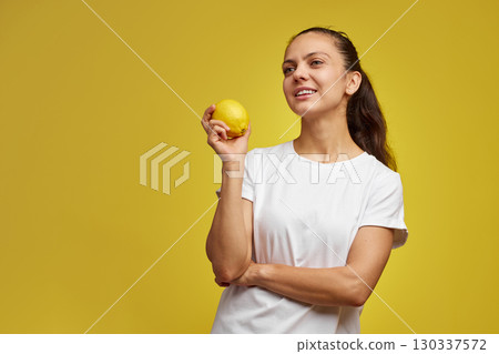 happy Caucasian woman holds fresh lemon on yellow background, vitamin fruit diet 130337572