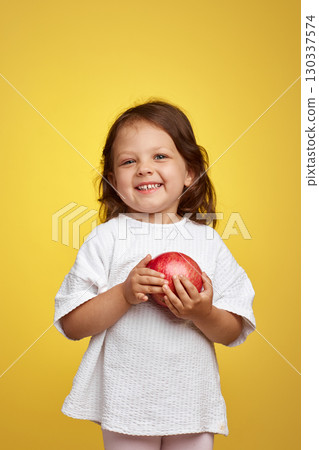 funny little child girl holding a pomegranate on yellow background. funny little child girl holding a pomegranate on yellow background. 130337574
