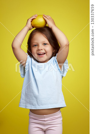 funny Caucasian little child girl holding lemon on yellow background 130337659
