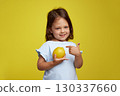 cute Caucasian little child girl pointing at lemon on yellow background 130337660