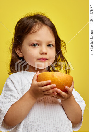 cute Caucasian little child girl holding grapefruit on yellow background cute Caucasian little child girl holding grapefruit on yellow background 130337674