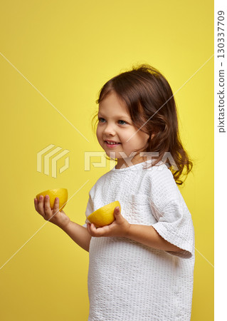 cute funny little child girl holding lemon on yellow background 130337709