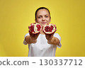 Beautiful happy woman holding pomegranate on yellow background, focus on pomegranate 130337712
