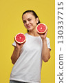 Happy Caucasian woman holds grapefruit halves on yellow background 130337715