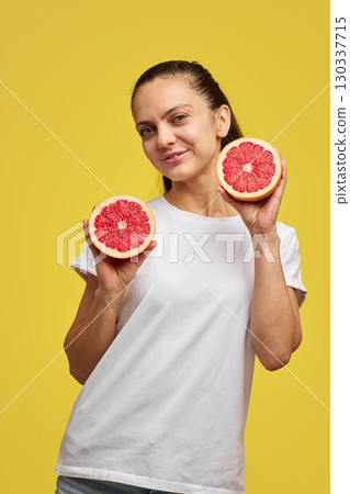 Happy Caucasian woman holds grapefruit halves on yellow background 130337715