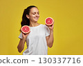 Happy Caucasian woman holds grapefruit halves on yellow background 130337716