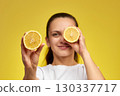 caucasian woman covering eyes with fresh lemon slice on yellow background, vitamin fruit diet 130337717
