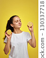 brunette woman holds fresh lemon slice on yellow background, vitamin fruit diet 130337718