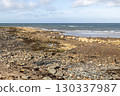 View of Rock and Stone Covered Beach with Blue Sea and Cloudy Sky on a Summer Morning 130337987