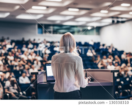 Female speaker giving a talk on corporate business conference. Unrecognizable people in audience at conference hall. Business and Entrepreneurship event Female speaker giving a talk on corporate business conference. Unrecognizable people in audience at conference hall. Business and Entrepreneurship event 130338310