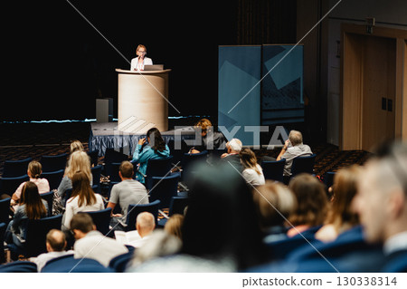 Female speaker giving a talk on corporate business conference. Unrecognizable people in audience at conference hall. Business and Entrepreneurship event 130338314