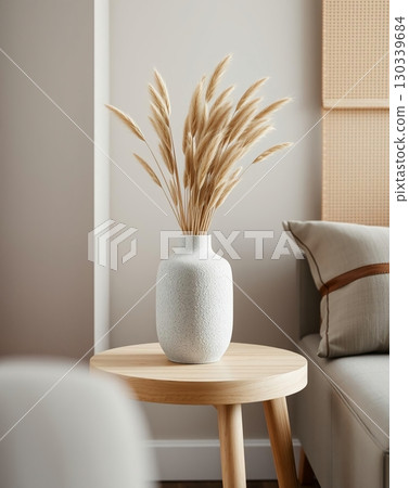 White vase with dried ornamental grass on a round wooden side table in a room White vase with dried ornamental grass on a round wooden side table in a room 130339684